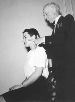 Frederick Mathias Alexander working with the head and neck of a seated woman using the Alexander Technique, a technique he developed.